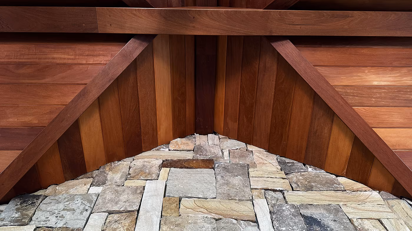 Close-up of a rustic wall combining natural stone masonry at the bottom and warm wooden paneling at the top, framed by angular wooden beams.