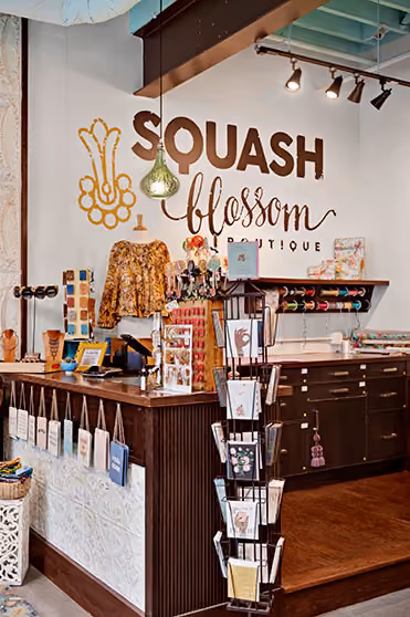 Interior of Squash Blossom Boutique with a display counter, gift cards, craft supplies, and a floral blouse on a mannequin.