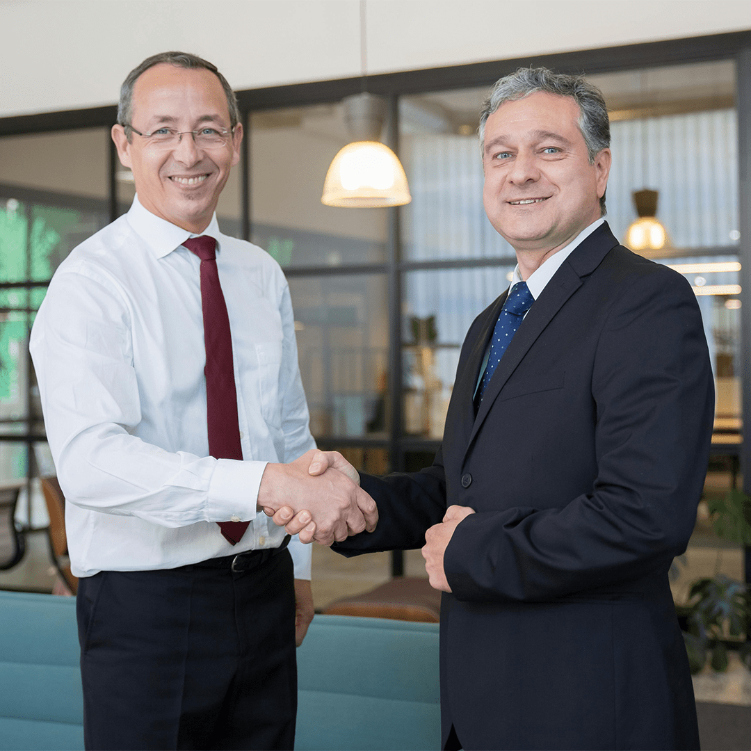 Two professional men smiling and shaking hands in a modern office setting.