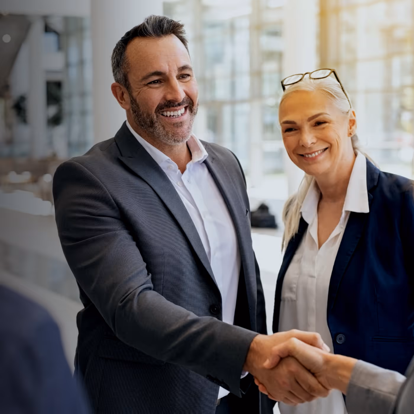 Smiling businesspeople shaking hands in a bright modern office while two colleagues look on.