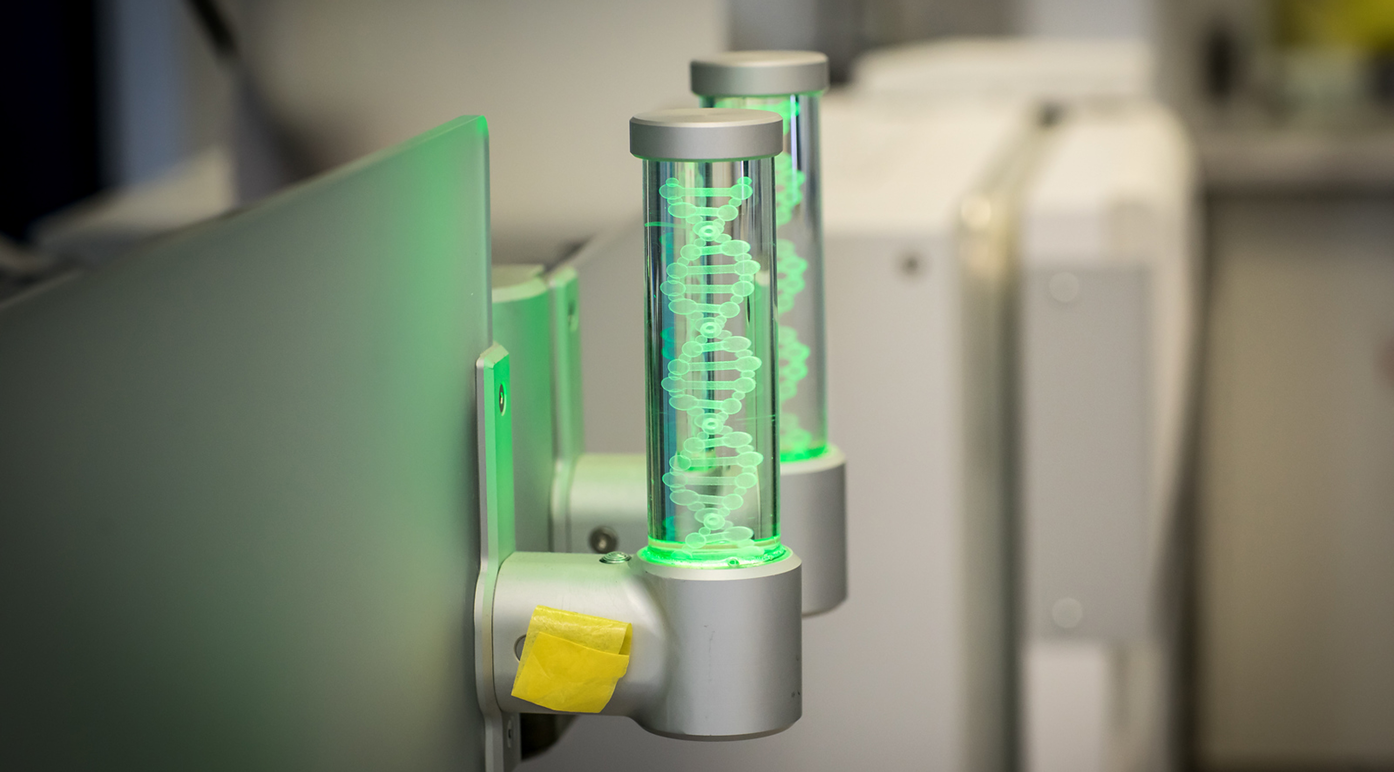 Two cylindrical light fixtures with green illuminated DNA helix designs mounted on a metallic surface.