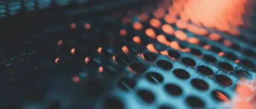 Close-up of a metal surface with evenly spaced circular holes illuminated by orange and blue light.