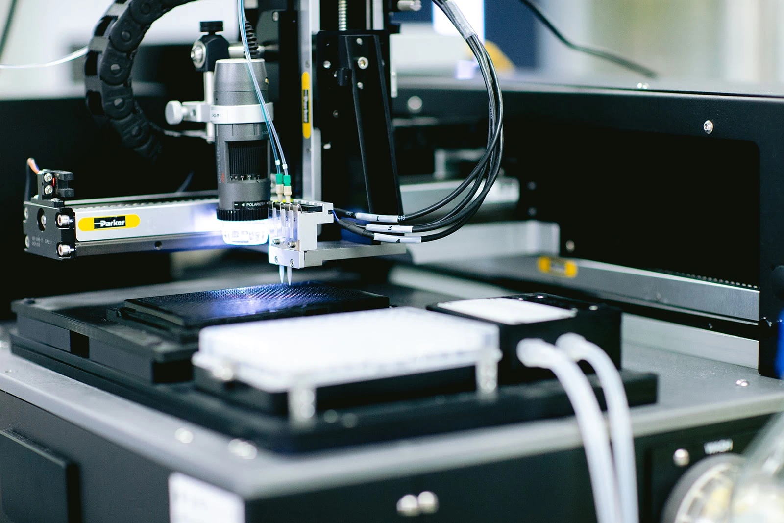 Automated laboratory instrument with a precision dispensing system applying liquid spots on a black target plate under a small camera or sensor.