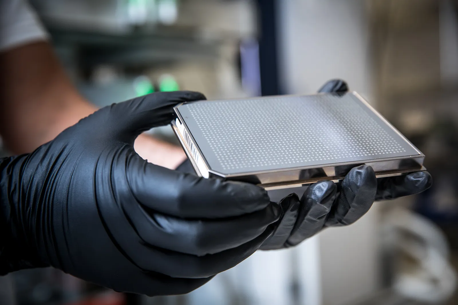Person wearing black gloves holding a metallic device with a perforated surface.