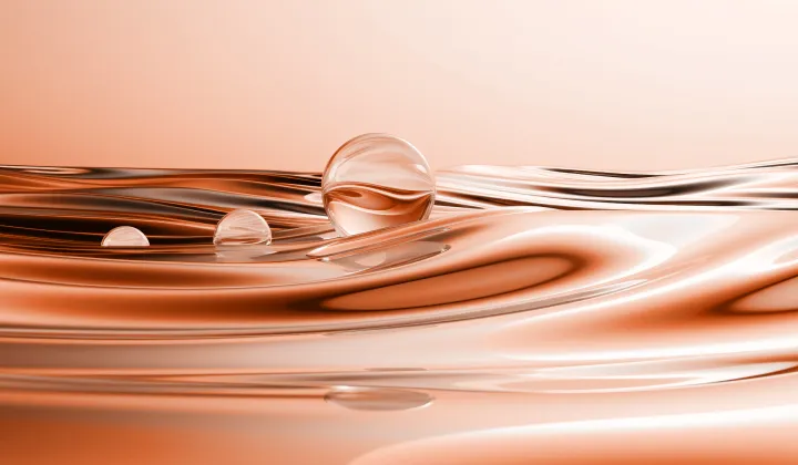 Three transparent water droplets rest on smooth, flowing copper-colored liquid surface.