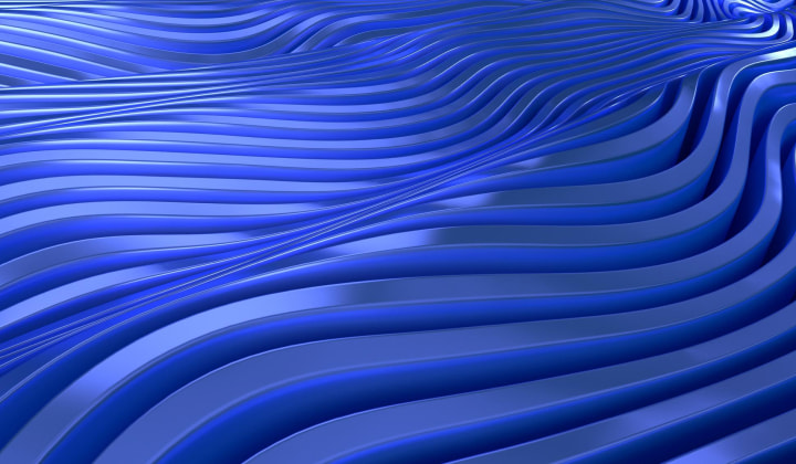 Young woman with dreadlocks and tattoos working on a laptop in a cozy kitchen, while a man in a brown hoodie reaches for something on a shelf in the background.