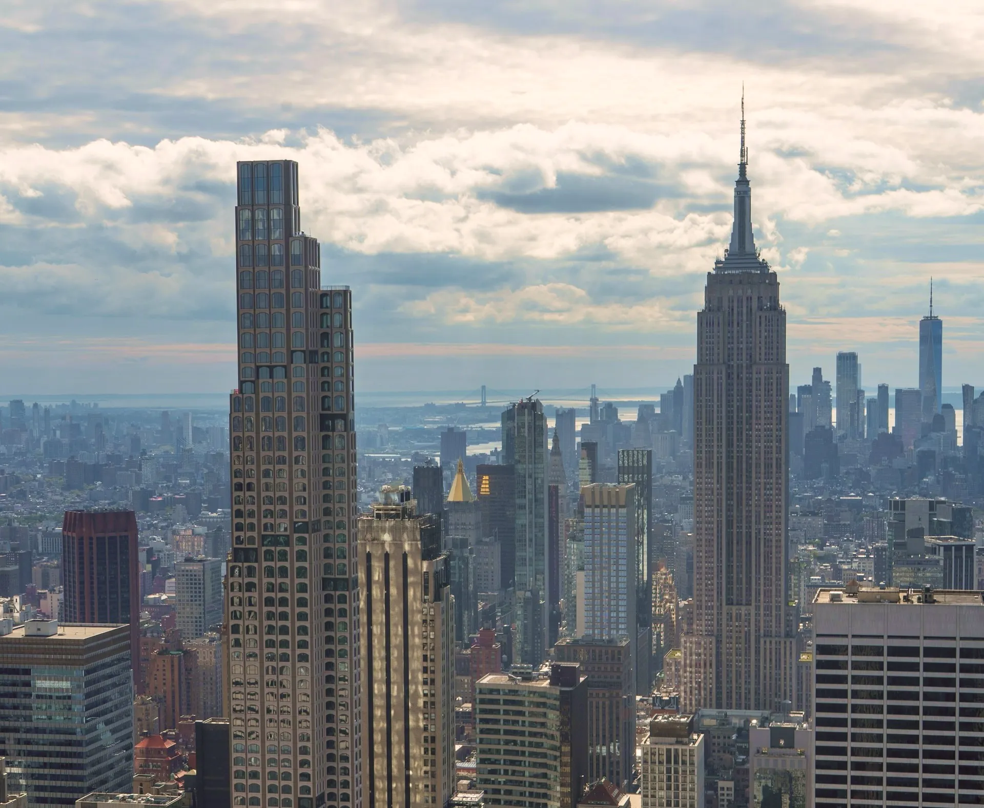 New York City skyline with the Empire State Building prominently in view under a cloudy sky.