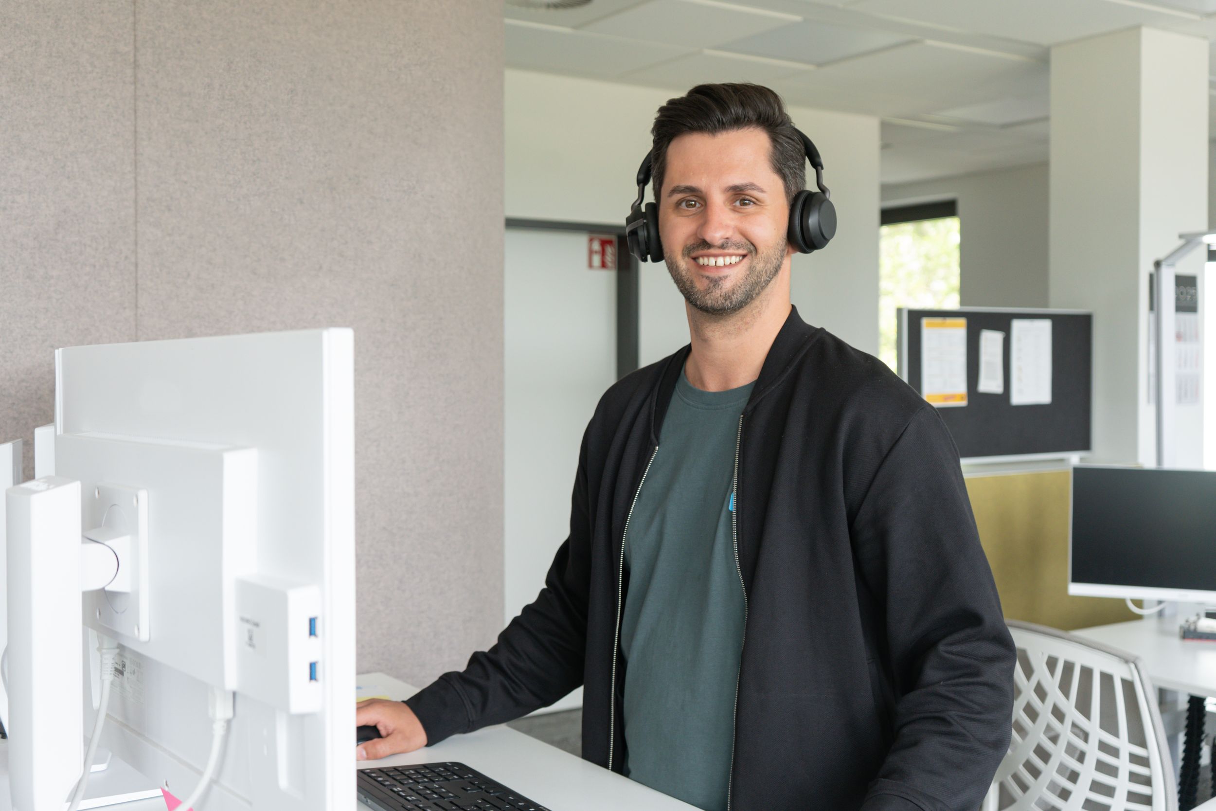 Lächelnder Mann mit Kopfhörern arbeitet an einem Computer in einem modernen Büro.