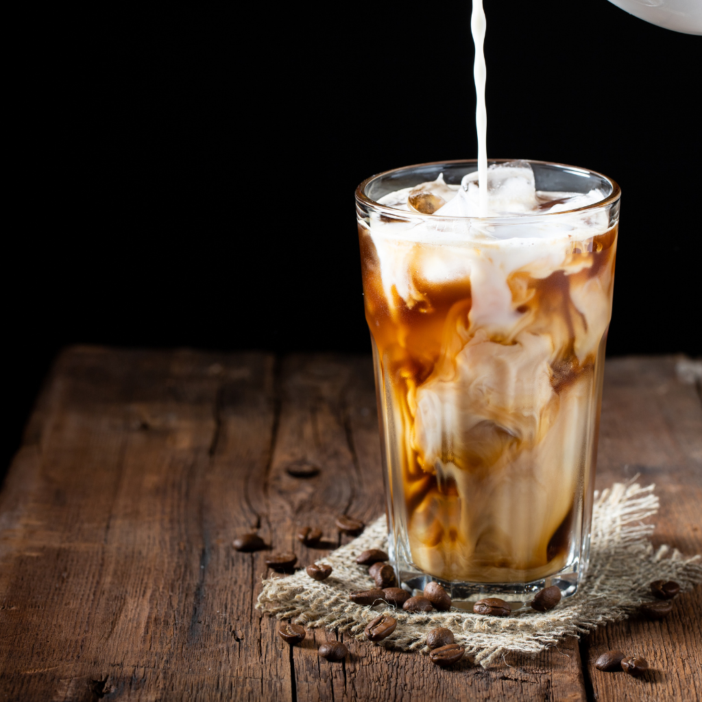 Cream or milk being poured into a cup of iced coffee.