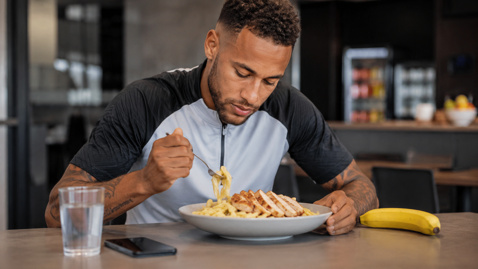Soccer player eating a pregame meal of pasta with chicken and a banana on the side, an example of carbohydrate-focused pregame fueling for competitive athletes