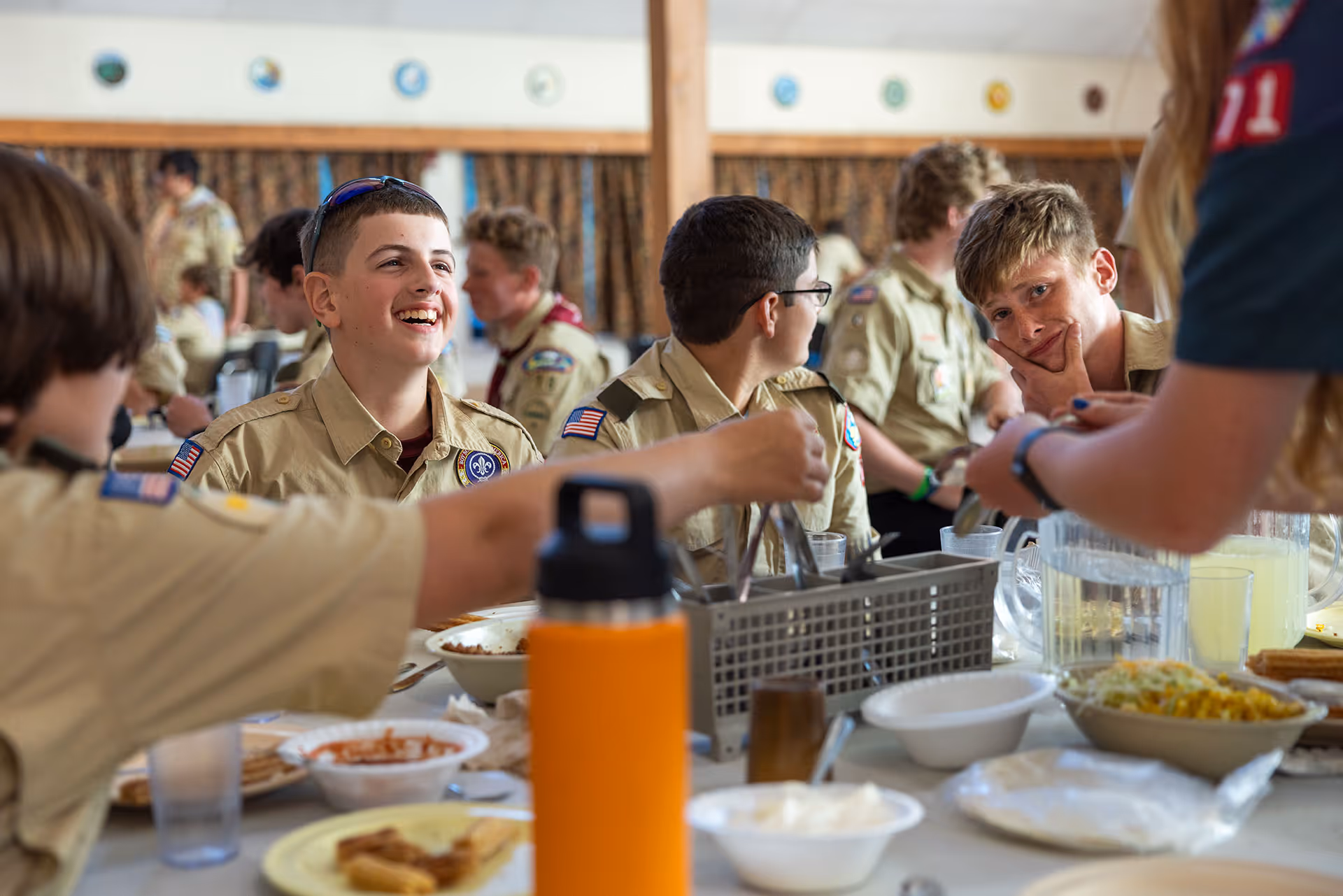 Group of Boy Scouts in uniform sitting at a table enjoying a meal together indoors.
