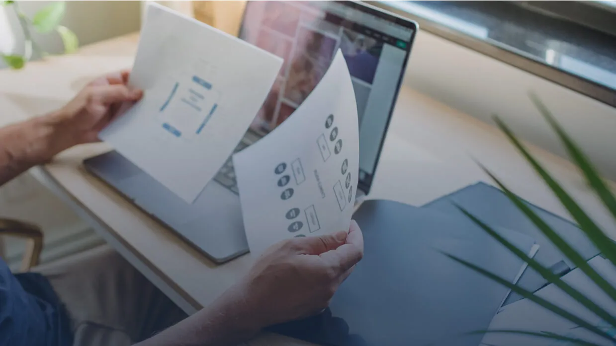 A person reviewing printed reports beside a laptop