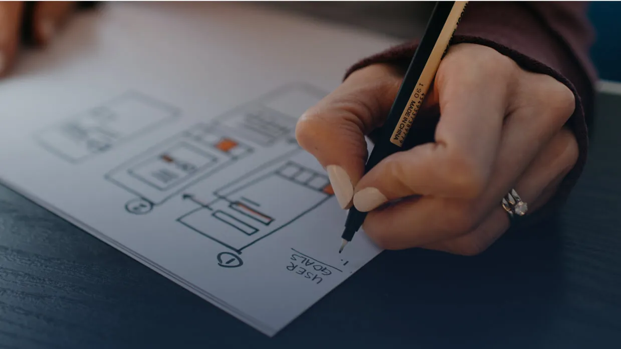 A hand sketching a website layout with a pen