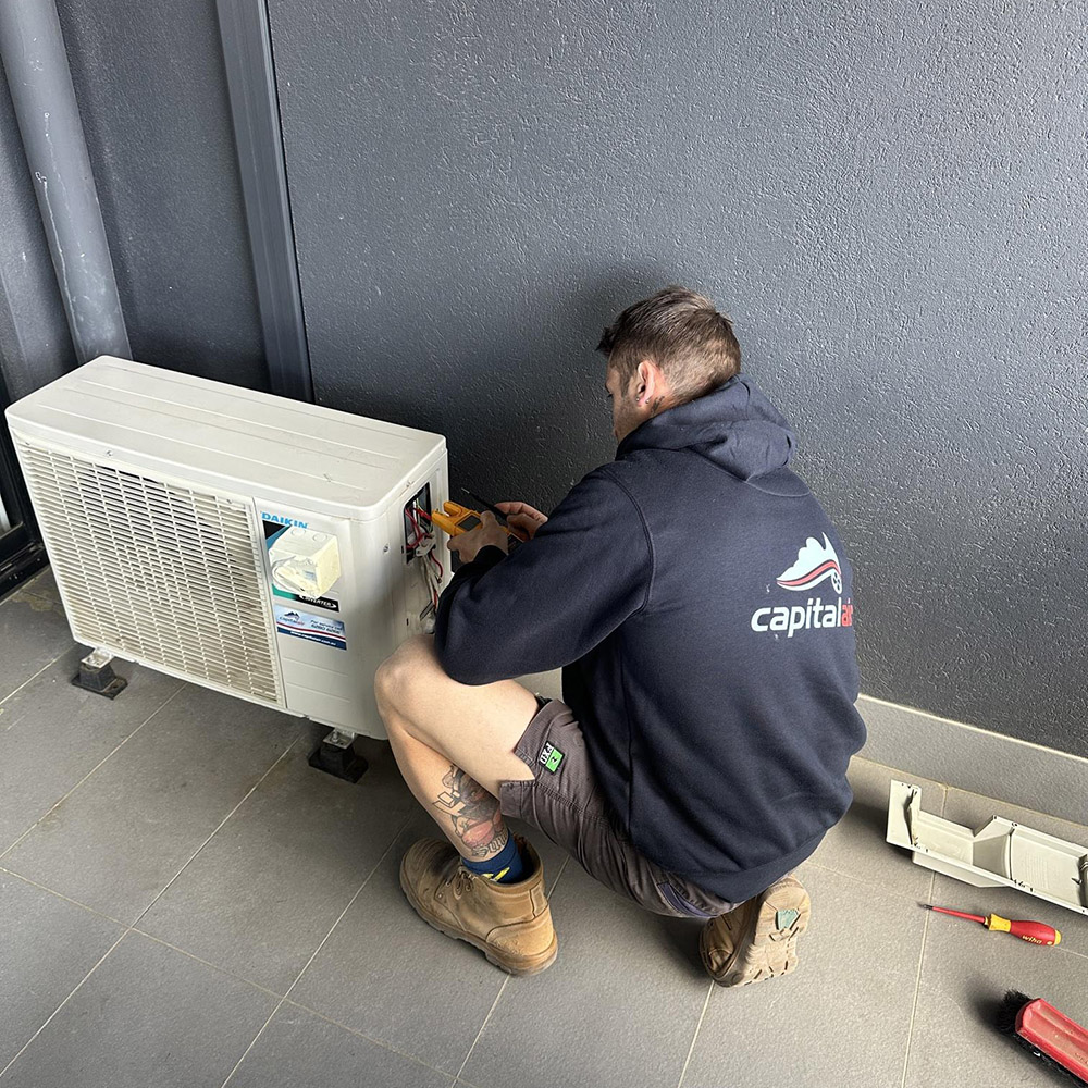 Capital Air technician connecting and testing an outdoor air conditioning unit.