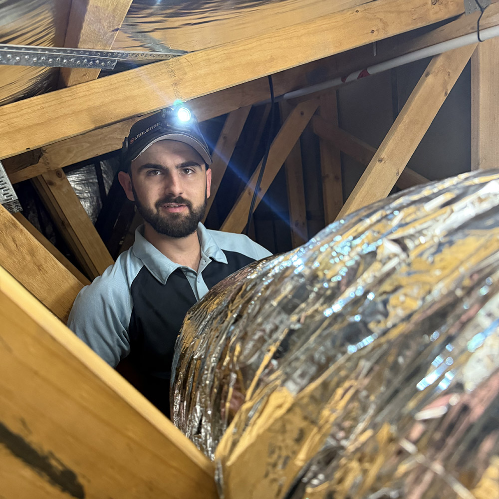 Capital Air Group technician checking ductwork inside a roof cavity.