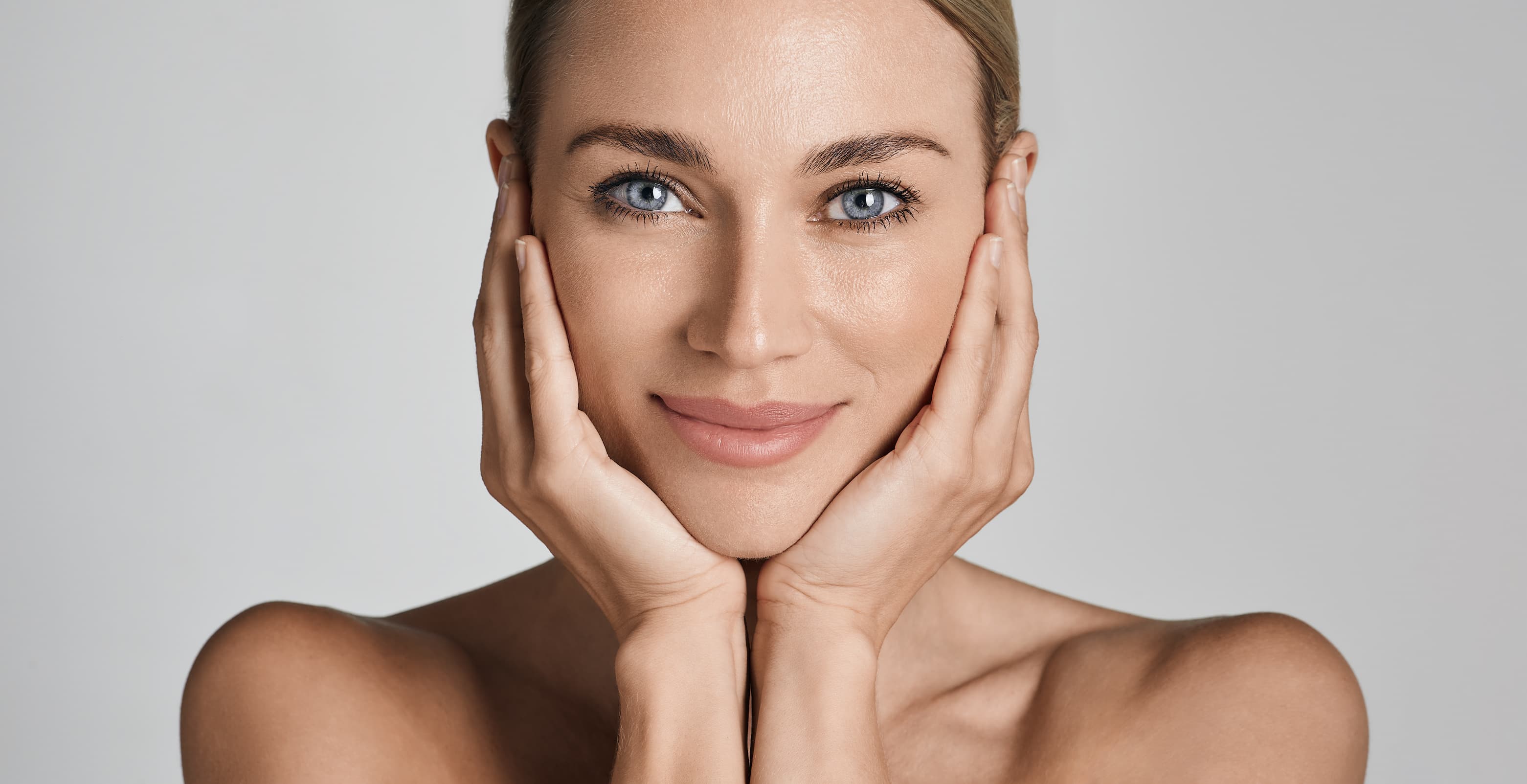 Portrait of a young woman with short wavy platinum blonde hair and blue eyes wearing a beige sleeveless top.