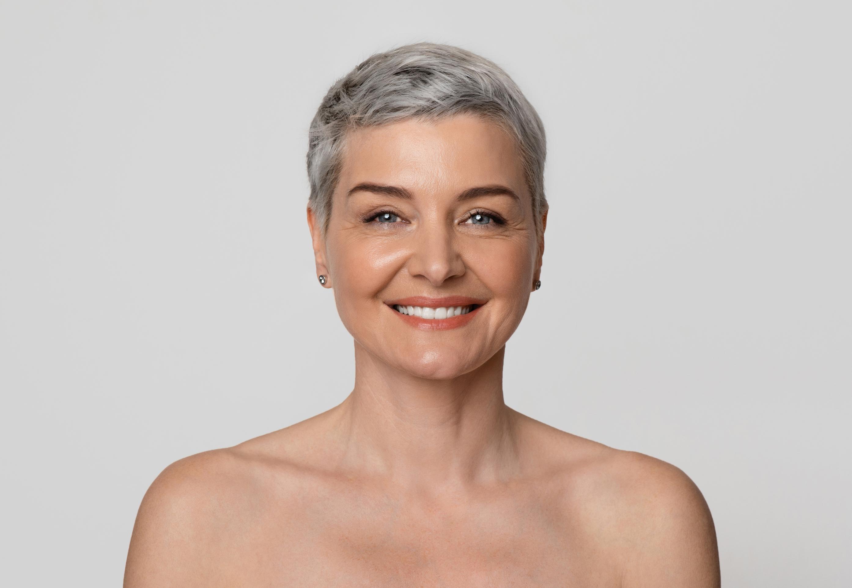 Woman in a white bikini posing against a textured beige wall with hands on hips.