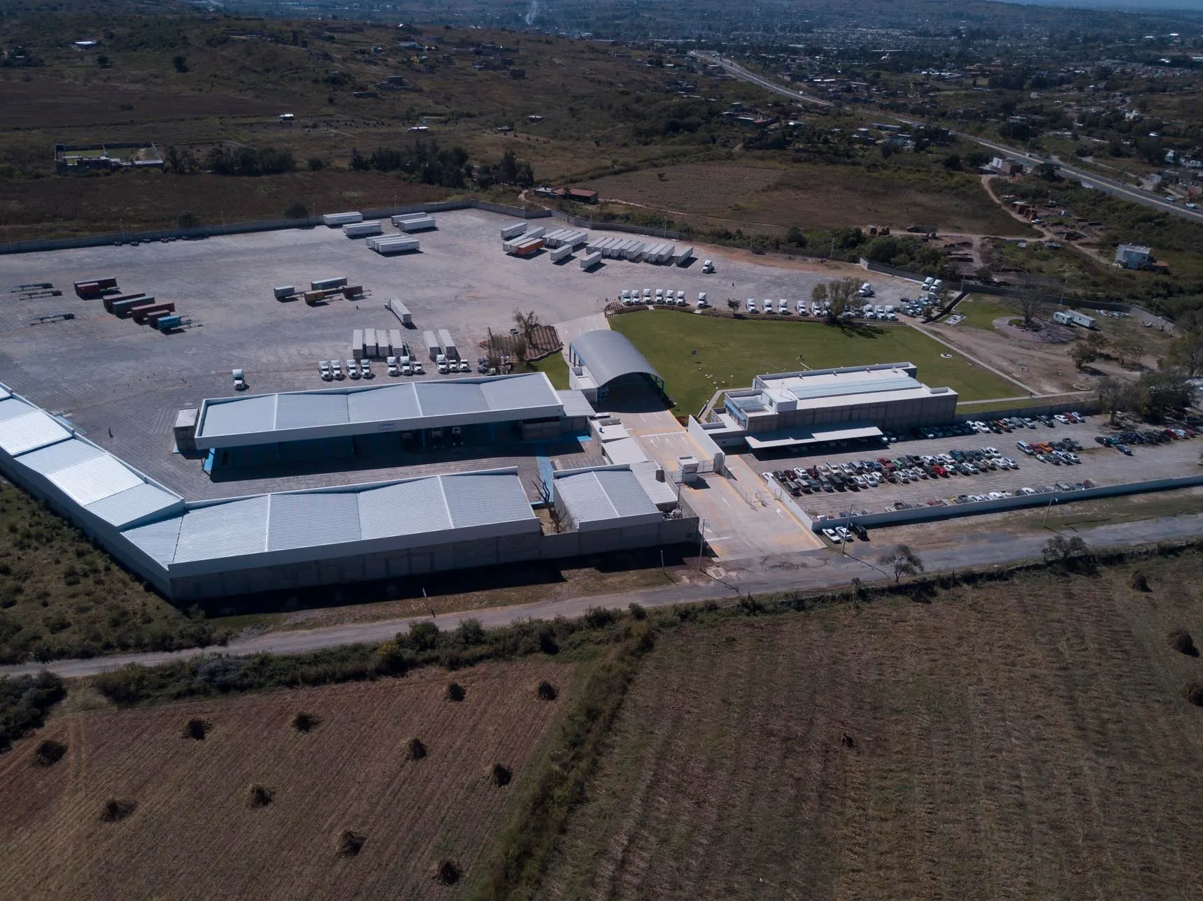 A wooden stool on the beach holding a glass of yellow drink and a small glass, with sun loungers in the background and sand underfoot.
