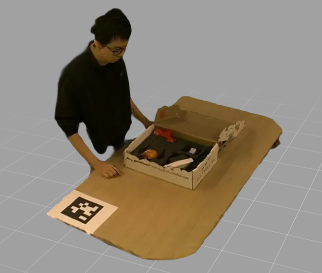 Person standing next to a cardboard box on a table containing various items including clothing and accessories.