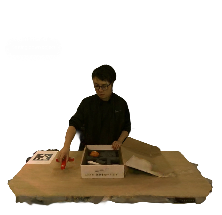 Person wearing glasses and a black top reaching with their left hand toward a red object on a wooden table, with a box labeled 'LEAR ROBOTICS' nearby.