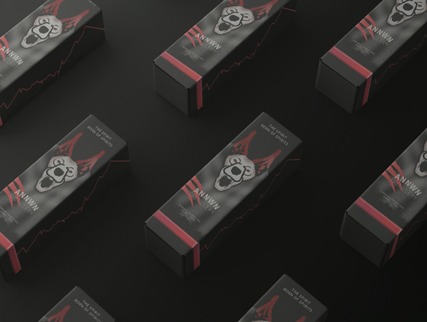 Black rectangular boxes featuring an illustrated dog face with red ears and the text 'ANNWN DISTILLERY' and 'THE SPIRIT BORN OF SPIRITS' on a dark background.