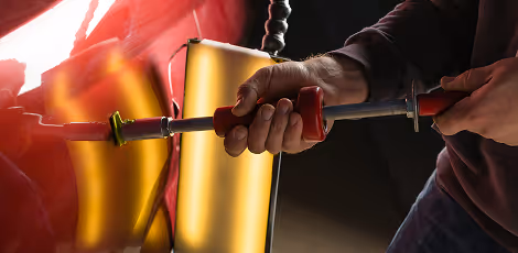 Person using a red-handled tool to fix or adjust a component with glowing heating elements.
