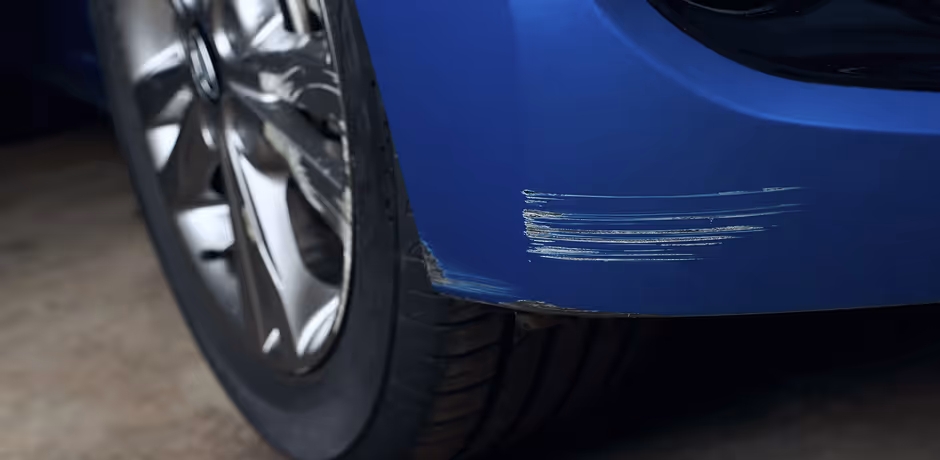 Close-up of a blue car's rear wheel and bumper with visible scratches and scuff marks.