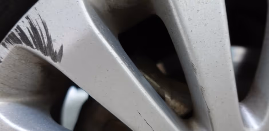 Close-up of a car wheel rim with visible scratches and scuff marks on the silver surface.