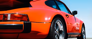 Red classic sports car with shiny chrome wheels parked under clear sky.