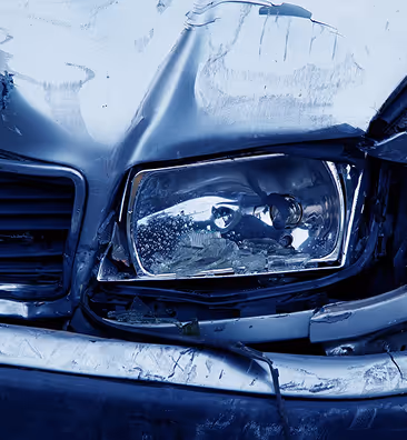 Close-up of a damaged car front showing a broken headlight and dented hood.