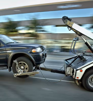 Black SUV being towed by a tow truck with blurred city background.