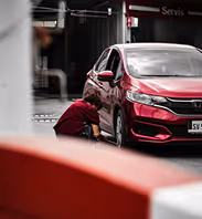 Man kneeling and inspecting the front wheel of a red car near a service center.