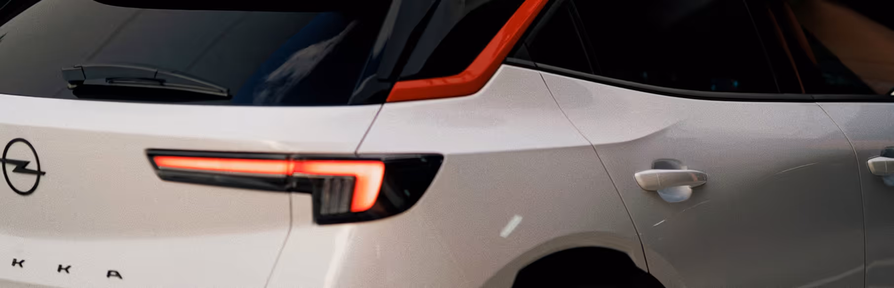 Close-up of the rear side of a white Opel Mokka car with illuminated taillight and red accent near the rear window.