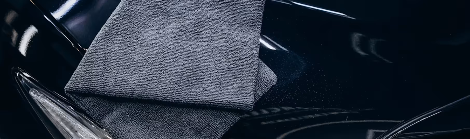 Grey microfiber towel folded on the shiny black surface of a car hood.