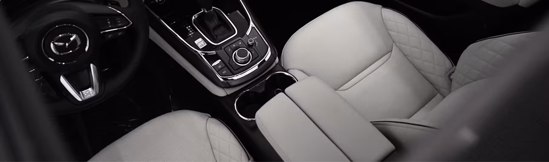 Interior view of a car showing beige leather front seats, center console with control buttons, gear shift, and cup holders.