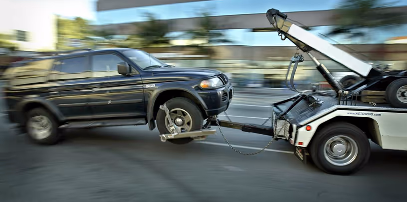 Black SUV being towed with its front wheels lifted and locked on a tow truck labeled Howard Sommers.