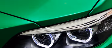 Close-up of a sleek green car’s modern dual LED headlights.