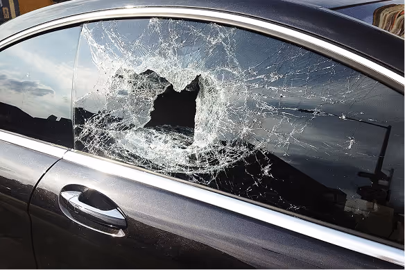 Car side window shattered with a large central hole and extensive cracks spreading outward.