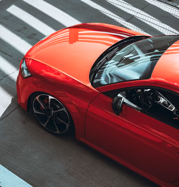 Top-down view of a shiny red sports car parked on a concrete surface with shadows from a grid overhead.