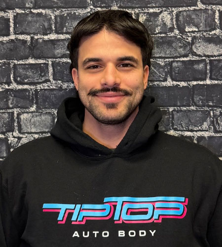 Man with mustache and short hair wearing a black Tip Top Auto Body hoodie standing in front of a brick wall.