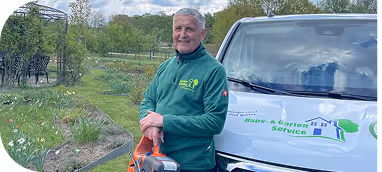 Älterer Mann mit grünem Pullover steht lächelnd neben einem Fahrzeug mit Haus- und Gartendienst-Logo.