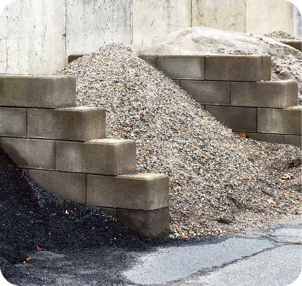 Drei unterschiedlich gefärbte Schutt- und Kieshaufen, durch Betonblöcke getrennt.