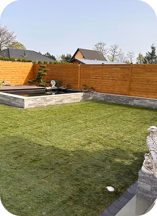 Moderner Garten mit gepflegtem Rasen, einem kleinen Teich mit Pflanzen und einer Holzzaunumzäunung im Hintergrund.