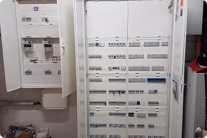 Elektrischer Sicherungskasten mit geöffneten Türen und verschiedenen Schaltern und Sicherungen an der Wand.