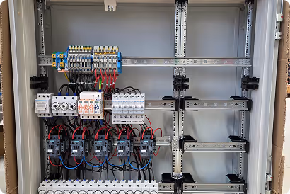 Geöffneter grauer Elektroschaltkasten mit mehreren Reihen von Schaltern, Relais und verdrahteten Anschlüssen.