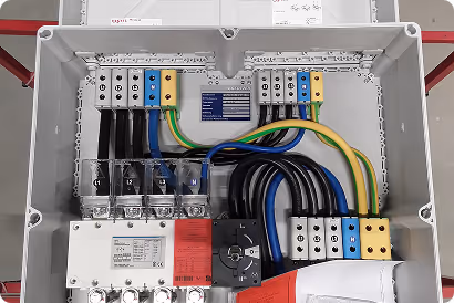 Offene Elektroverteilung mit bunten Kabeln und angeschlossenen Sicherungen in einem grauen Kasten.