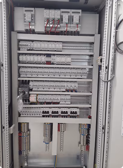 Innenansicht eines offenen elektrischen Schaltschrankes mit mehreren Reihen von Sicherungen, Relais und Verdrahtungen.