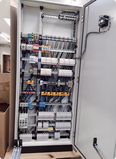 Offenes elektrisches Schaltschrankgehäuse mit mehreren Reihen von Verdrahtungen, Sicherungen und Schalteinrichtungen in einem technischen Raum.