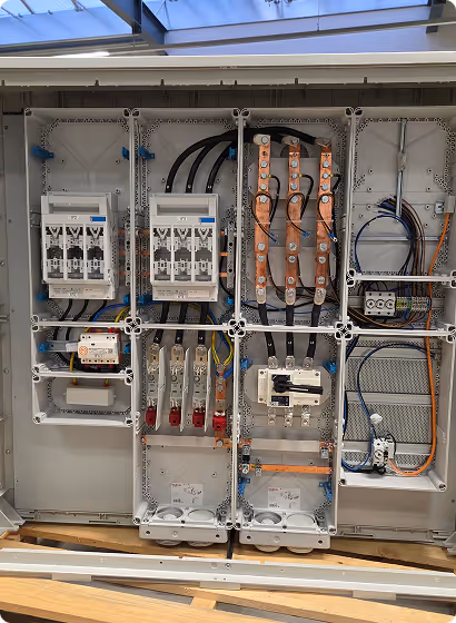 Innenansicht eines elektrischen Sicherungskastens mit sichtbaren Kabeln, Sicherungen, Kupferschienen und Steckern.
