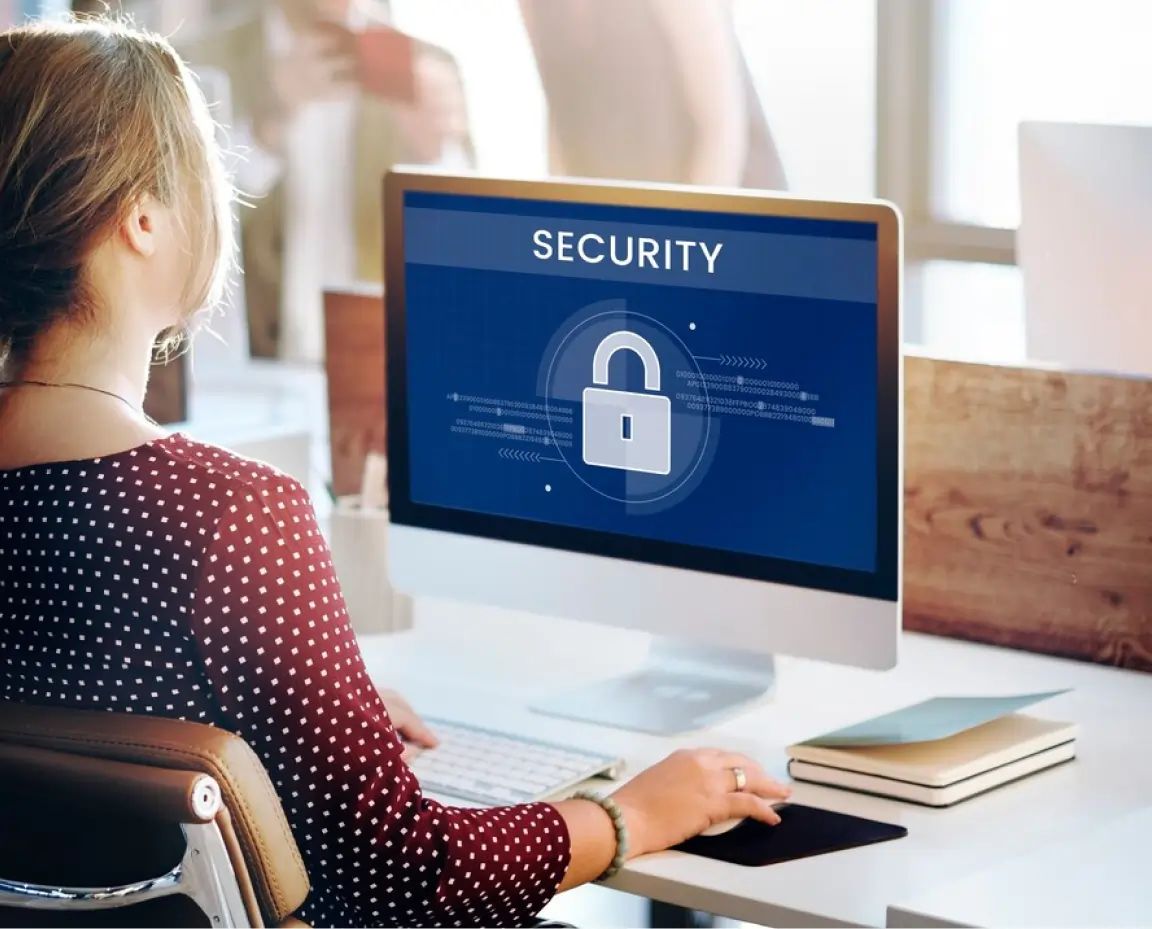Person sitting at a desk looking at a computer screen displaying a security padlock icon and the word 'SECURITY'.